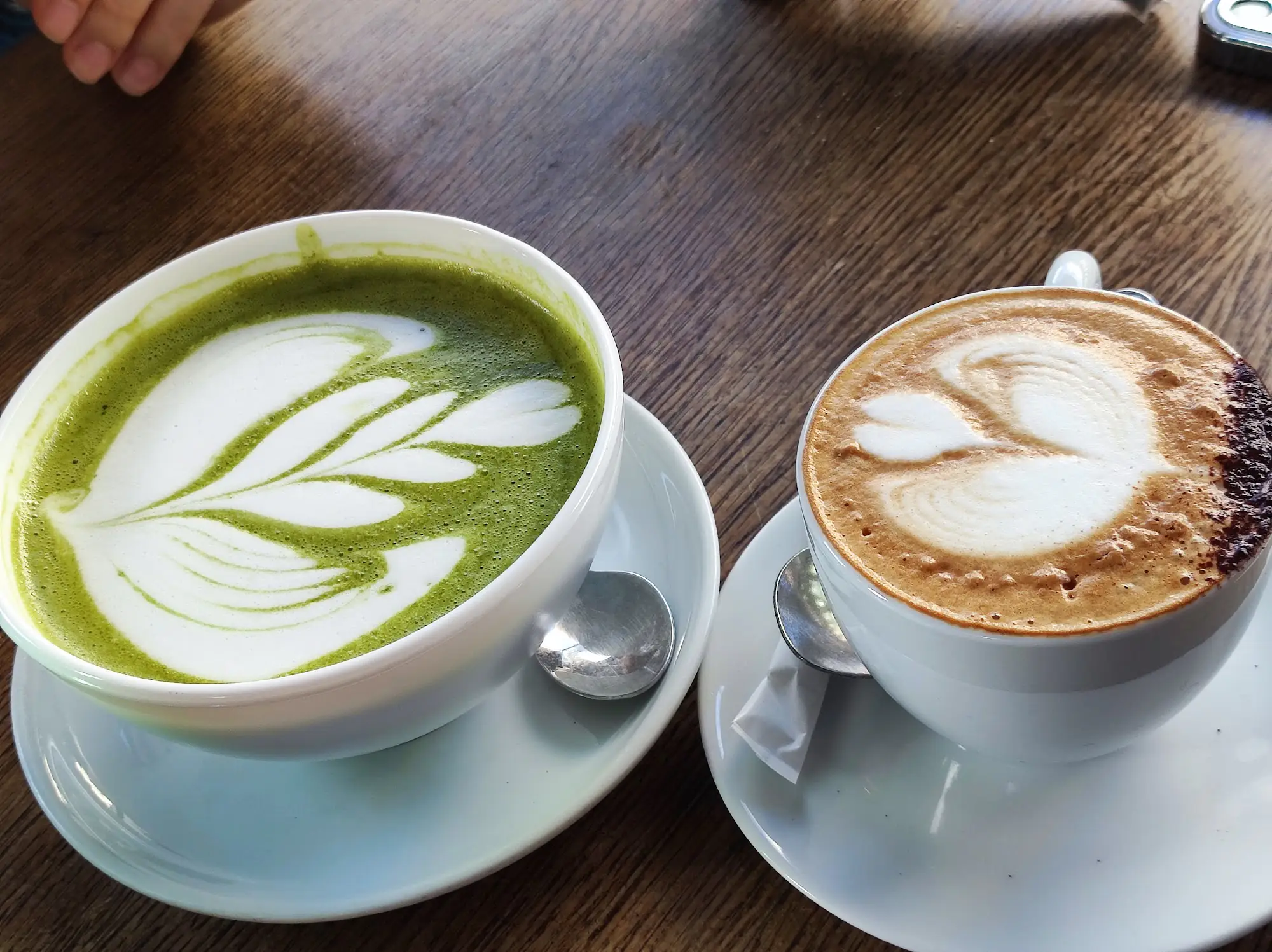 Zwei Heißgetränke mit Latte Art von oben, Matcha Latte und Espresso Latte